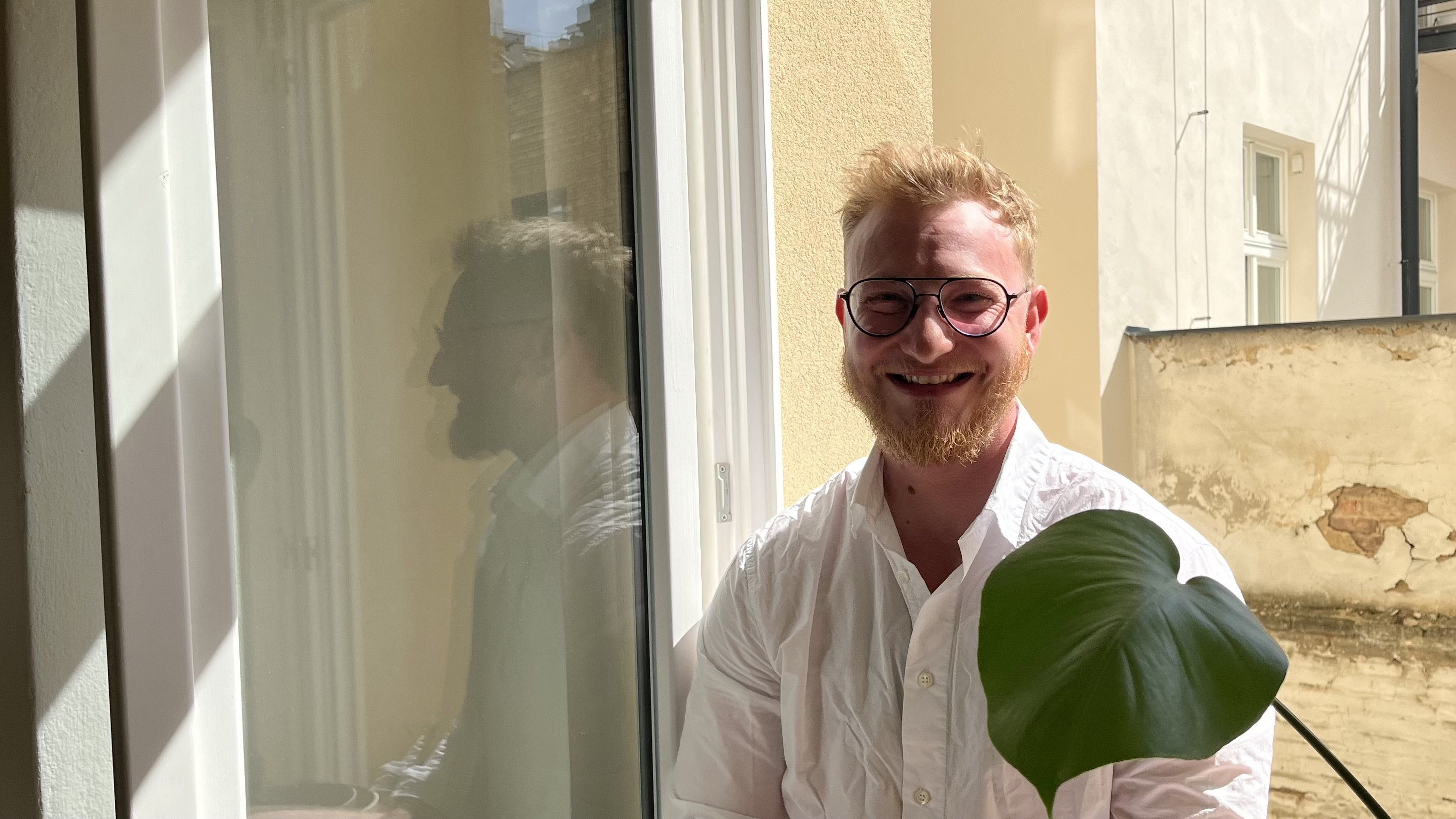 Jan Vacha smiling warmly, holding a plant leaf by a sunlit window