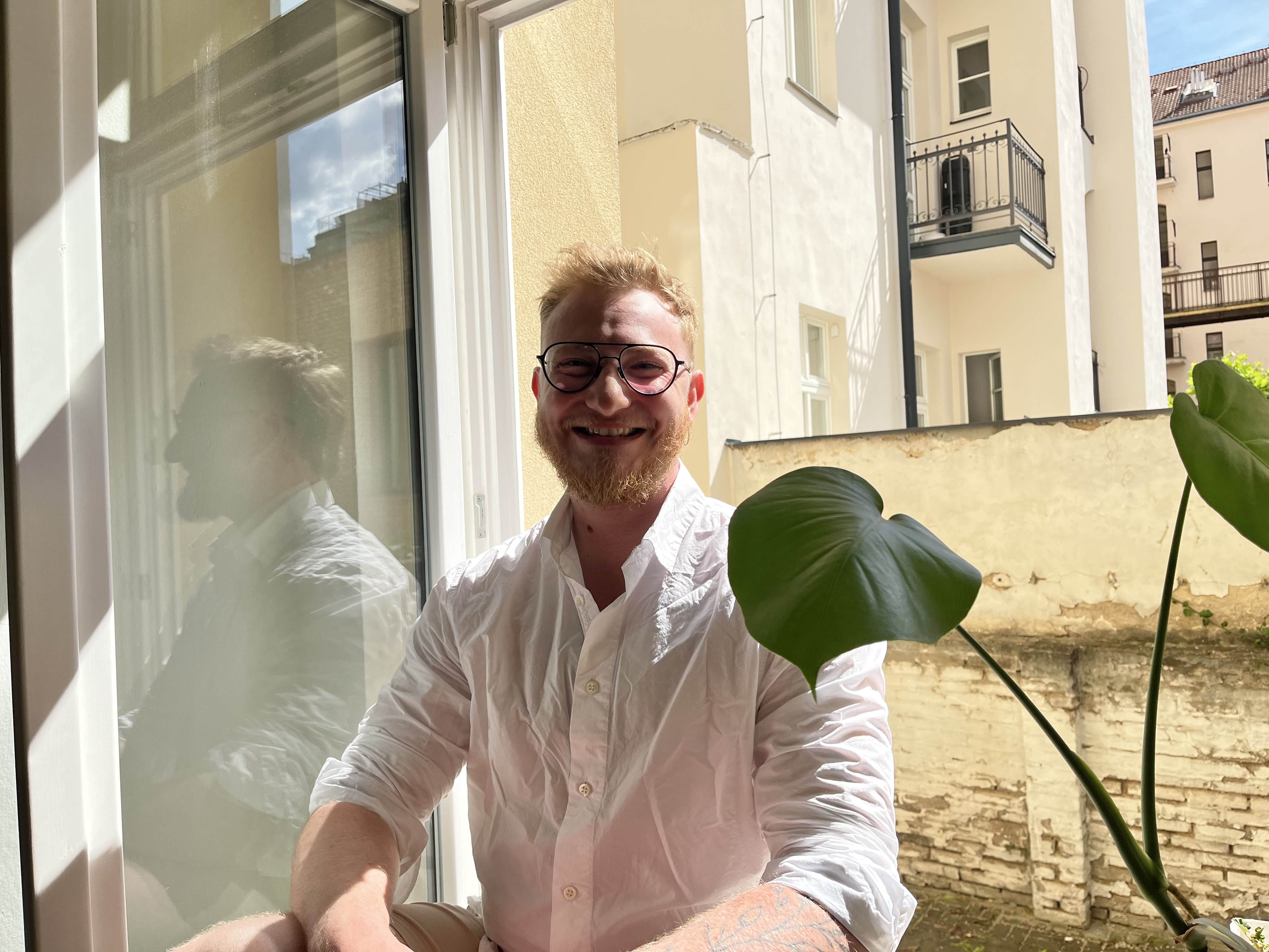 Jan Vacha smiling warmly, holding a plant leaf by a sunlit window